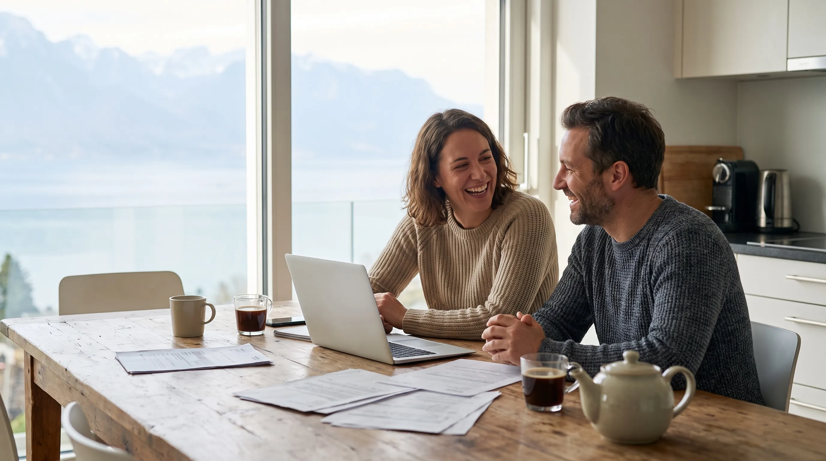 Un couple souriant compare ses primes sur un ordinateur, vue sur le Léman